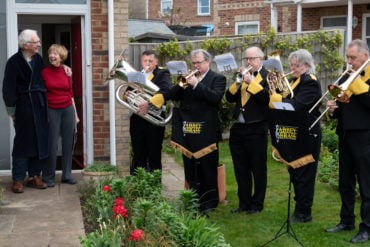 Mike and Penny Redman standing on their doorstep whilst members of Abbey Brass play live to them in their garden