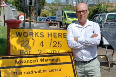 Andrew Garratt standing by road works sign