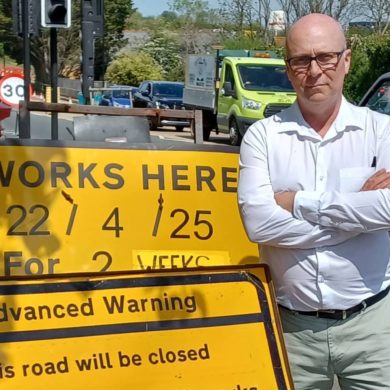 Andrew Garratt standing by road works sign