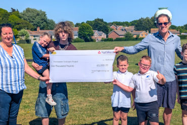 Parish Clerk Kirsty Gibson and Toby Jacobson, Contracts Manager, Trant Engineering Limited with a cheque for £1,000 with excited children who just happened to be on Stroud with their parents at the time