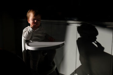 dark photo of a baby in a high chair pulling a face