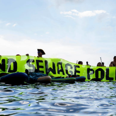 end sewage pollution banner being held up by paddleboarders in the water