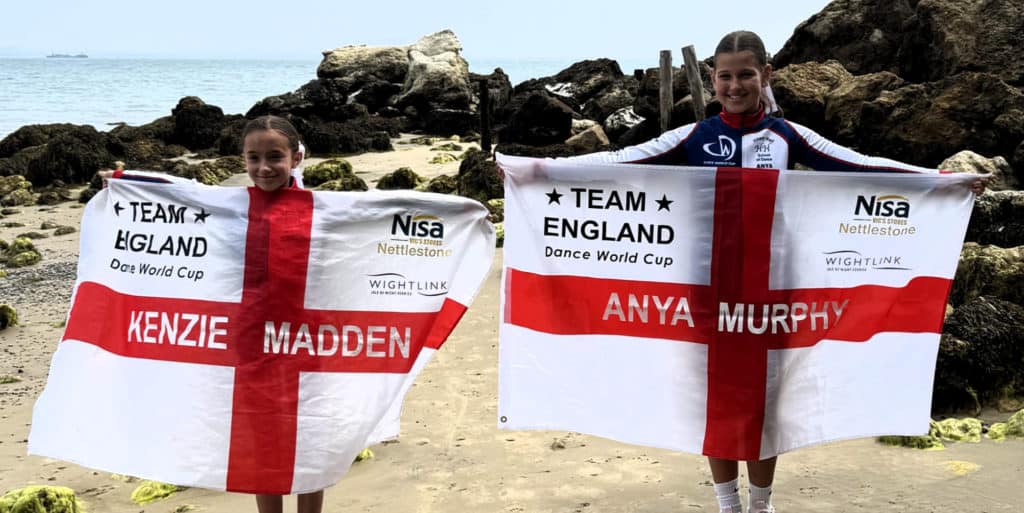 Anya and Kenzie standing on the beach holding Team England flags
