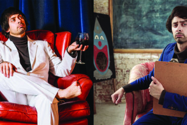 Marcel Lucont in a chair with a glass of wine and Marcel also sitting on another chair with a painting of a clown next to him