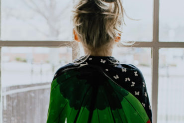 young girl looking out of the window, dressed in a peacock cape