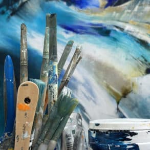 Artists paint brushes in front of coastal painting