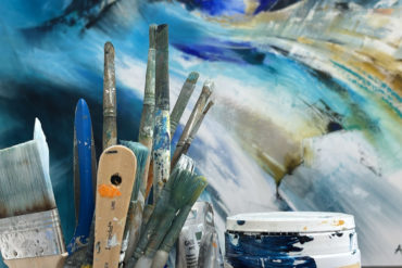Artists paint brushes in front of coastal painting