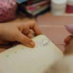 Child's hand drawing a flower in a notebook