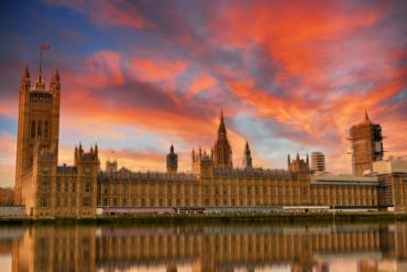 Palace of Westminster with pink sunset behind it and reflections on the river thames
