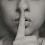 black and white photo of woman holding finger to mouth in shhing motion