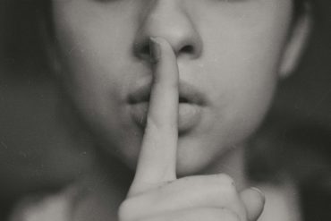 black and white photo of woman holding finger to mouth in shhing motion