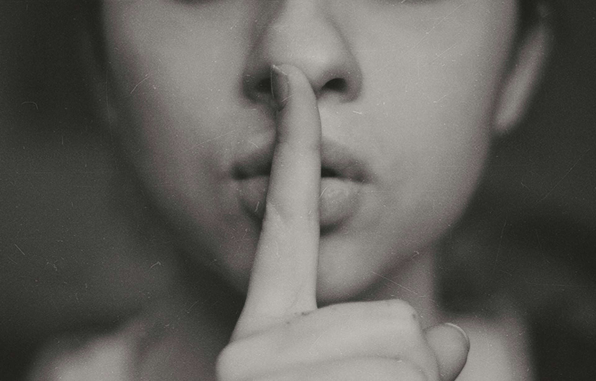 black and white photo of woman holding finger to mouth in shhing motion
