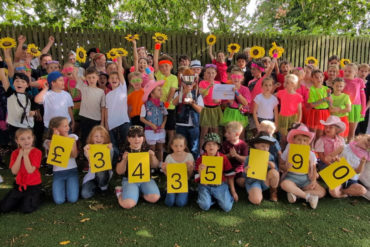 Pupils from Carisbrooke Primary holding sunflowers and large cards with the amount raised