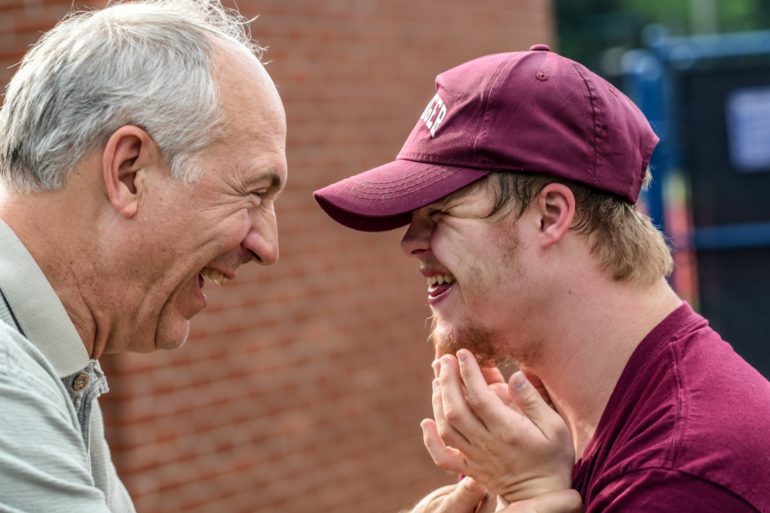 An older man smiling with a man with downs syndrome by nathan anderson