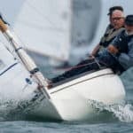 Astralita yacht sailing towards the camera with three sailors hanging off the side