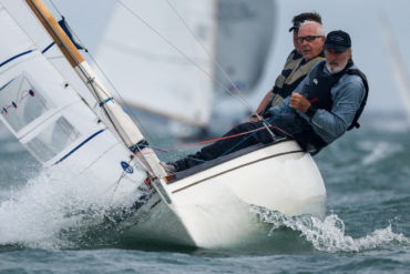 Astralita yacht sailing towards the camera with three sailors hanging off the side