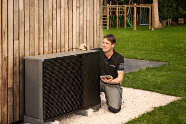 Daikin heat pump being serviced on side of a wooden clad house