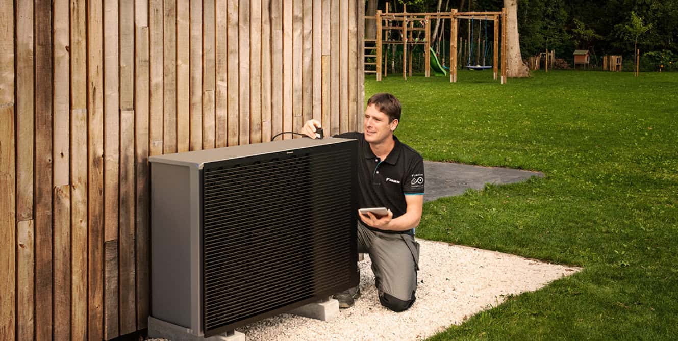 Daikin heat pump being serviced on side of a wooden clad house