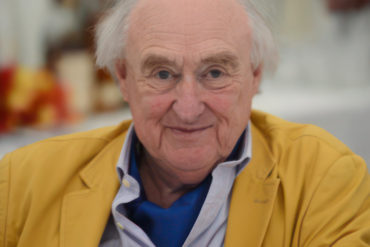 Henry Blofeld looking at the camera whilst wearing a canary yellow jacket