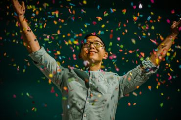 Person with arms in the hair as confetti falls against a dark background