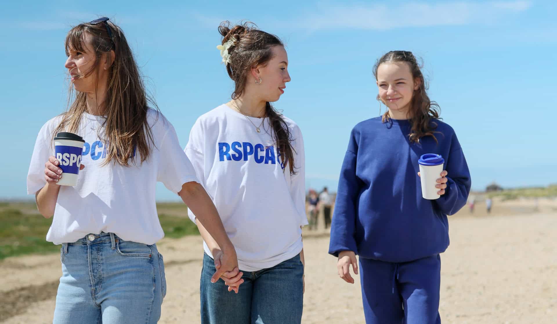 Three women walking on a beach wearing RSPCA T-shirts