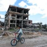 Boy riding a bicycle down a bombed Gazan street