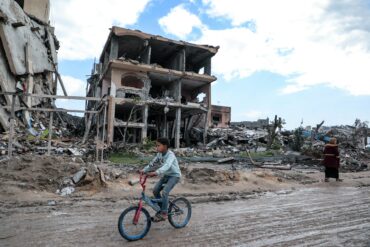 Boy riding a bicycle down a bombed Gazan street