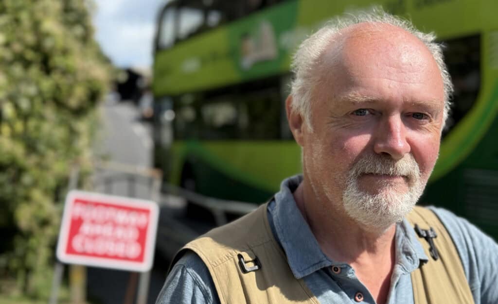 Martin Simpson with a bus going up the hill behind him