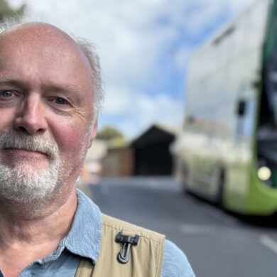 Martin Simpson with the bus coming down the hill behind him