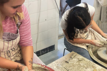 Two young women learning how to throw pottery on a potters wheel