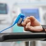 a person in hospital with their wrist bound to the bed, with their pulse being monitored