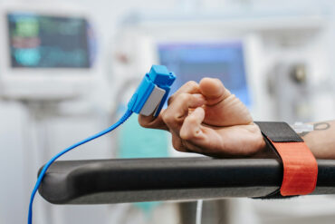 a person in hospital with their wrist bound to the bed, with their pulse being monitored