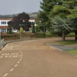 Photo of the school from the road, with lots of trees in the foreground and Downs in the background