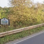 welcome to sandown sign by side of road with bushes and trees behind