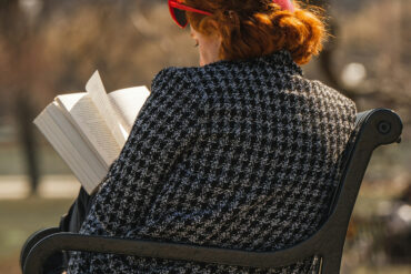 woman sitting on a bench in a park reading her book