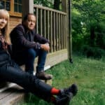 Charlie Dore and Julian Littman sat on the steps of a wood cabin