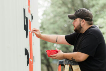 Man up a ladder painting a mural on a wall