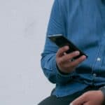 man in denim shirt sat down and looking at his mobile phone