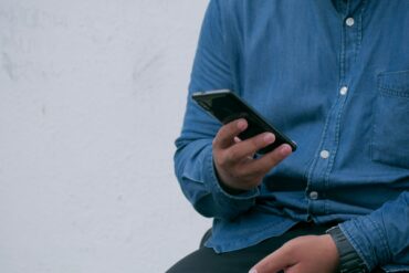 man in denim shirt sat down and looking at his mobile phone