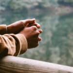 person leaning on a fence looking at a lake