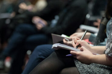 row of people at press conference writing notes in notebooks