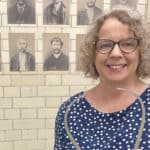 Dr Angela Buckley posing for the camera with Victorian mugshots on the wall behind her