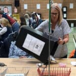 People at the election count, with officer tipping out postal votes onto the table ready for counting