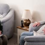 Lisa Beaney from Green Isle of Wight CIC sitting in a lounge talking to an older man who is sat in an armchair