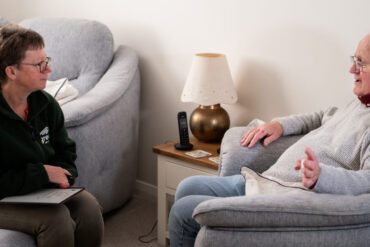 Lisa Beaney from Green Isle of Wight CIC sitting in a lounge talking to an older man who is sat in an armchair