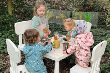 Four little girls sitting around a table in the woods