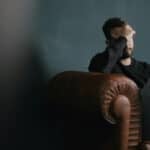 Man sitting on sofa in dark room holds hand over face