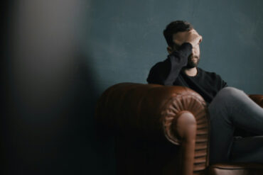 Man sitting on sofa in dark room holds hand over face
