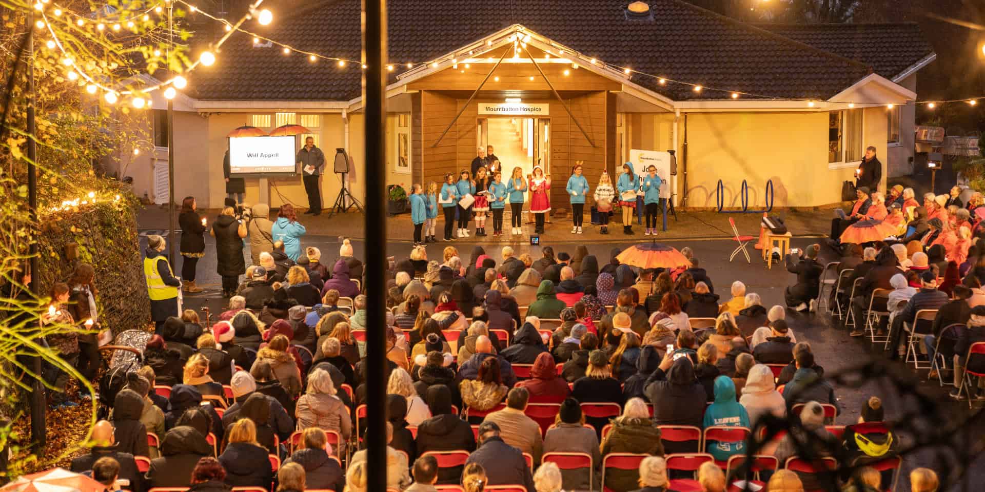 Mountbatten's Light up a life event with children ringing bells in front of a seat audience outside the hospice building