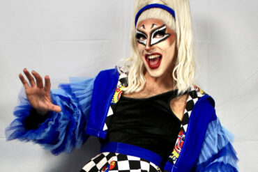 Quivers in drag makeup and bright blue outfit